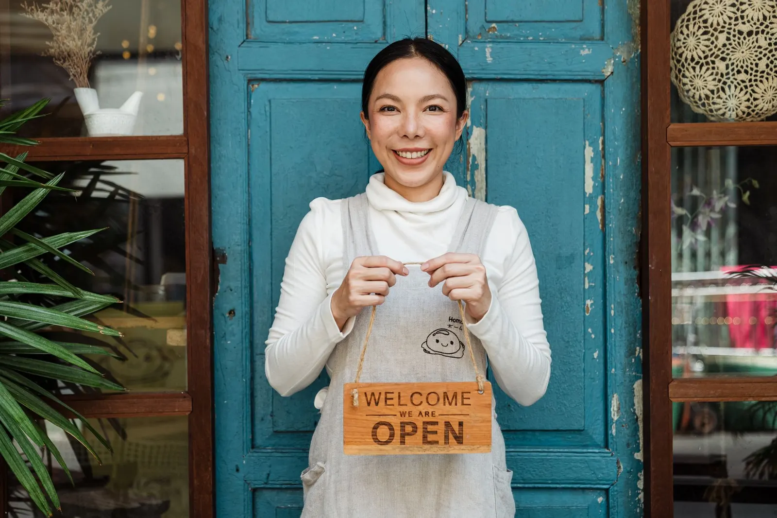 Propietaria de una cafetería sujetando un cartel de abierto en la puerta de su local