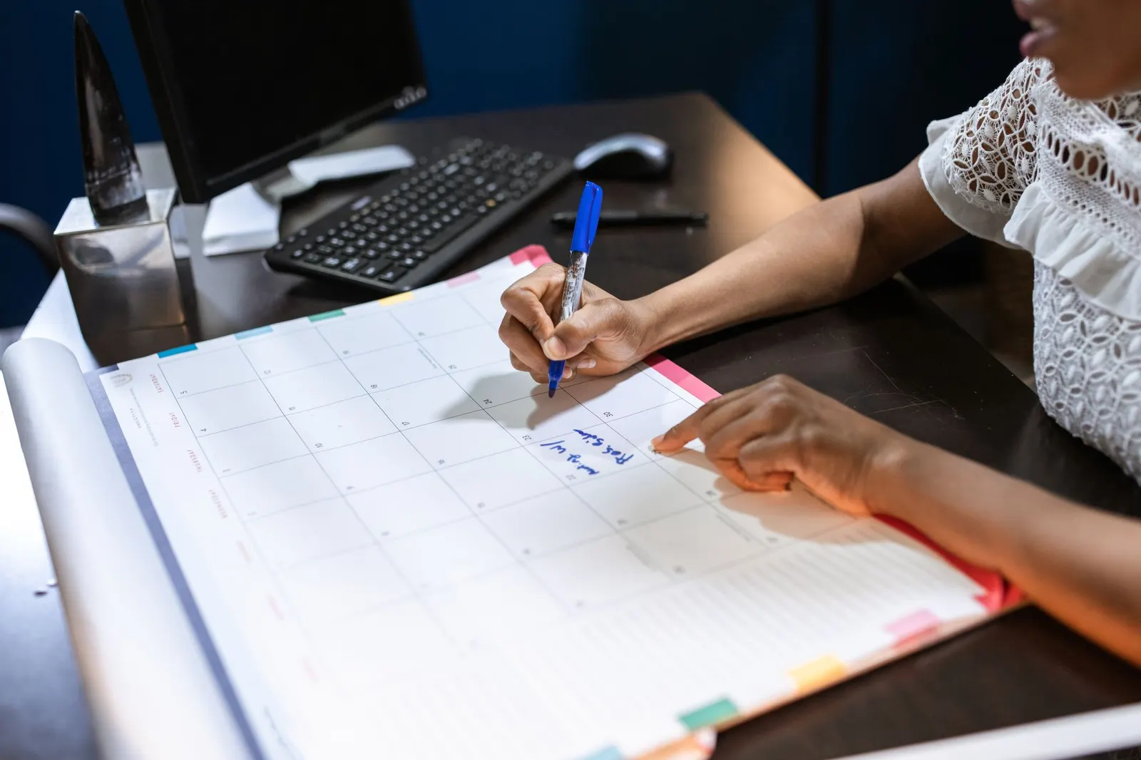 Persona anotando fechas en un calendario de escritorio con un bolígrafo