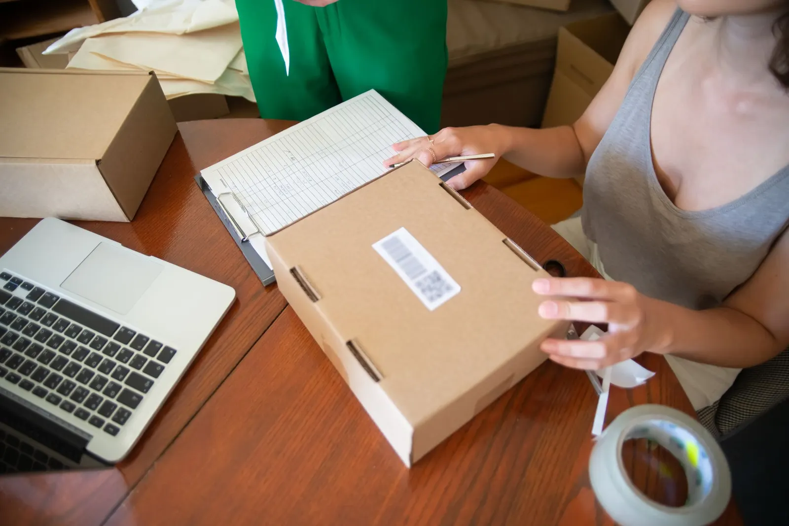 Mujer preparando un pedido en una caja de cartón junto a un ordenador portátil
