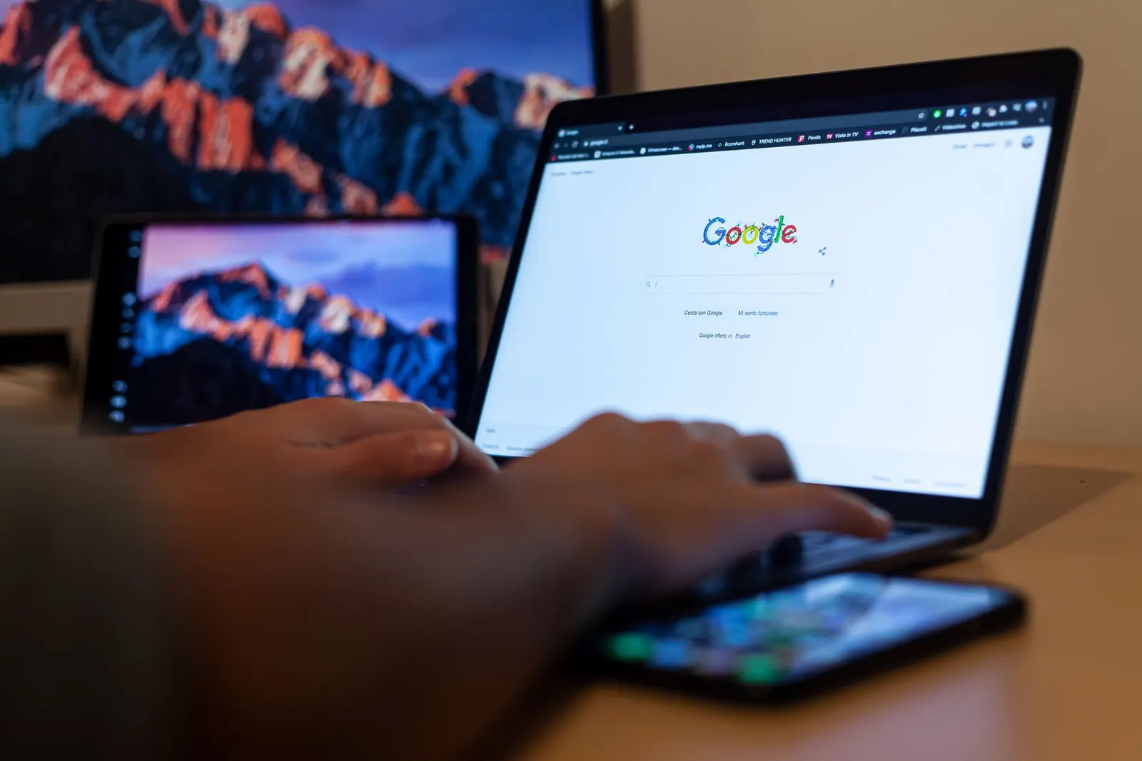 Persona escribiendo en un portátil con la página de inicio de Google abierta y un móvil sobre el teclado